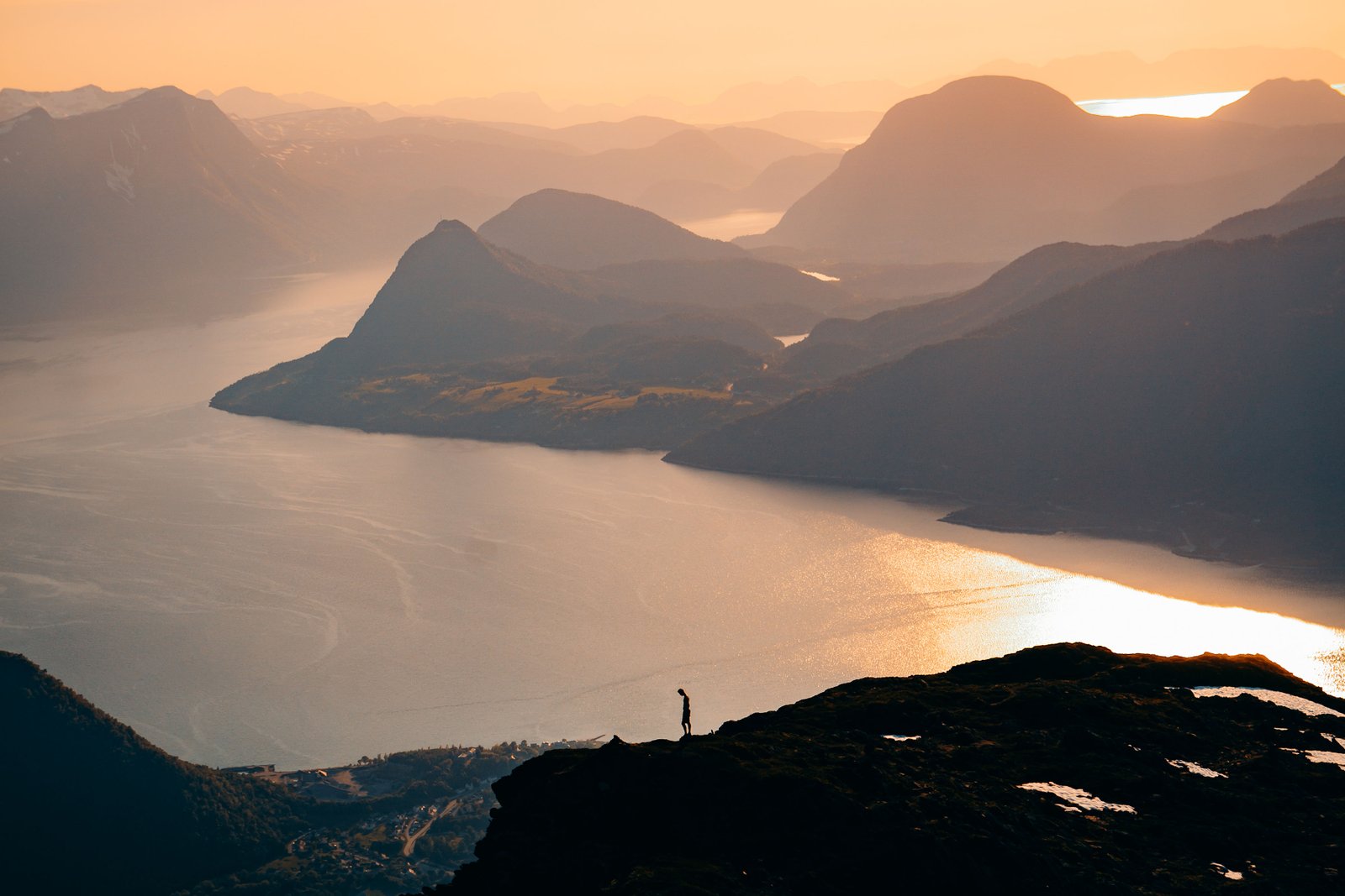 A lone figure on a high cliff above a fjord at golden hour